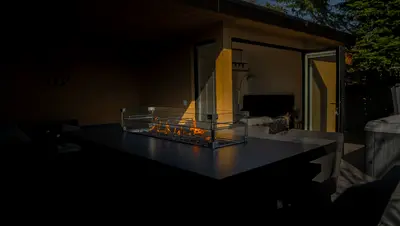 A fire table glowing in the evening outside a lit garden room