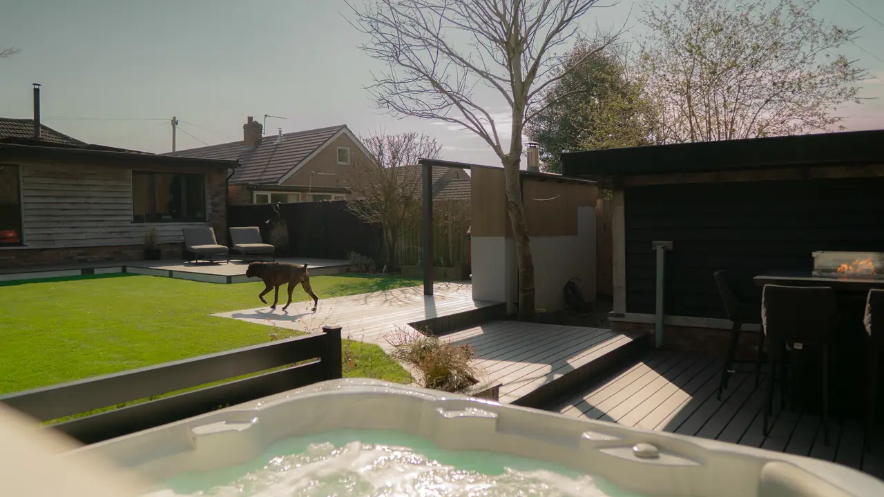 Looking over a hot tub across a grey deck to the lawn and garden room