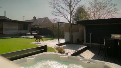Looking over a hot tub across the deck to the lawn, with a dog crossing the grass