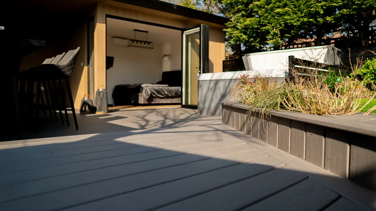A garden room with its doors open, the deck running up to it beside a raised planter