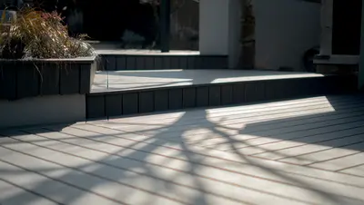 Deck steps and a raised planter, with tree shadows across the boards