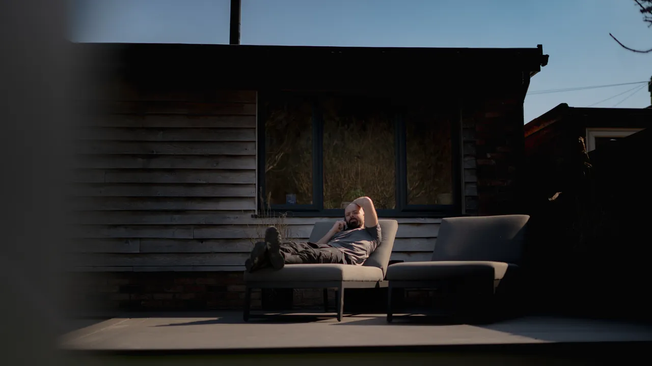 Someone resting on an outdoor sofa in the shade beside the garden room