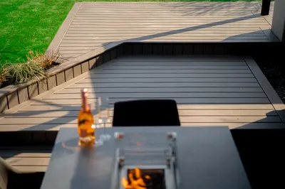A table with a bottle and glasses, looking down a stepped deck to the lawn