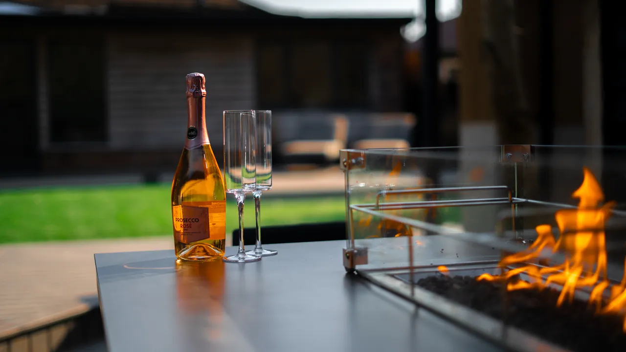 A bottle and two glasses beside the flames of a fire table