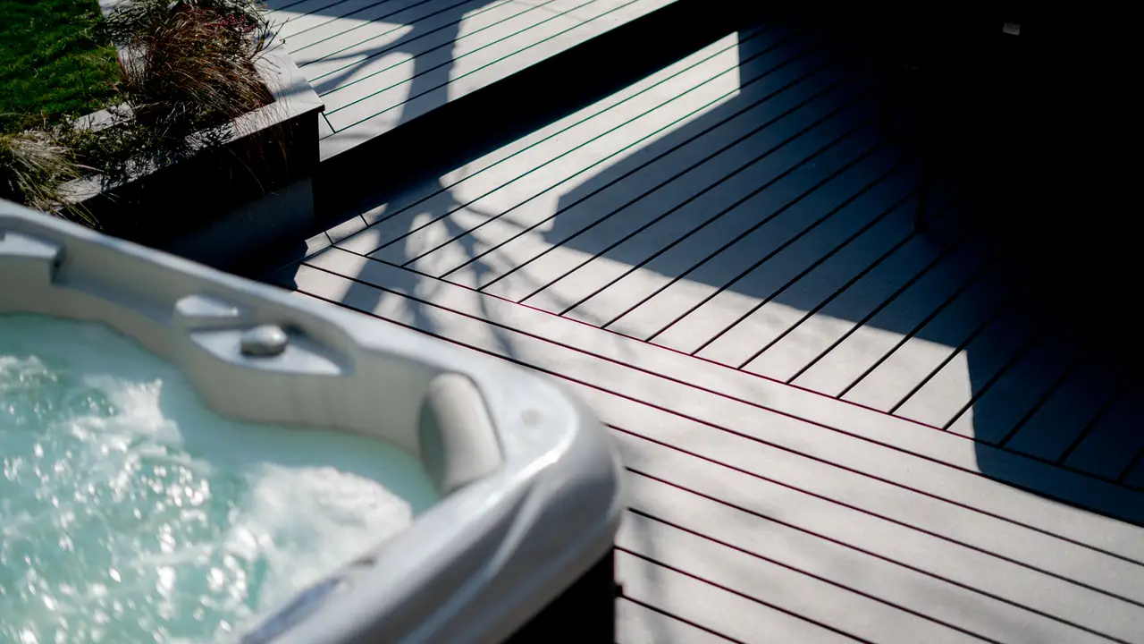 The corner of a hot tub over grey deck boards in strong sun