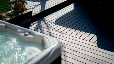 The corner of a hot tub over grey deck boards in strong sun