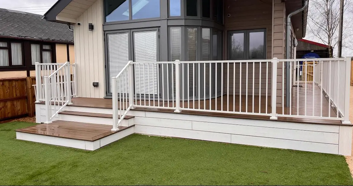 A Trex Enhance deck in Toasted Sand wrapping a holiday lodge, with white Trex Signature railing, white fascia and steps to the lawn