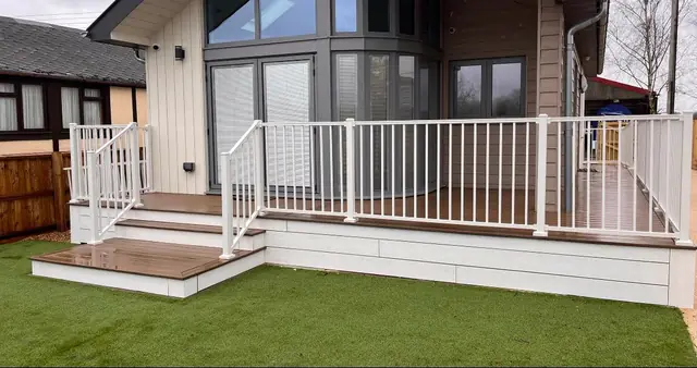 A Trex Enhance deck in Toasted Sand wrapping a holiday lodge, with white Trex Signature railing, white fascia and steps to the lawn