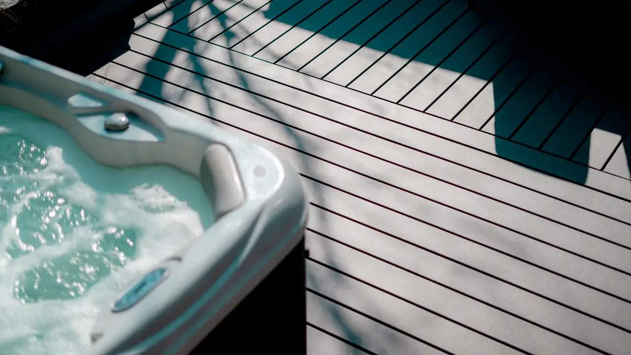 A hot tub set into a grey Trex deck, low sun casting long shadows across the boards