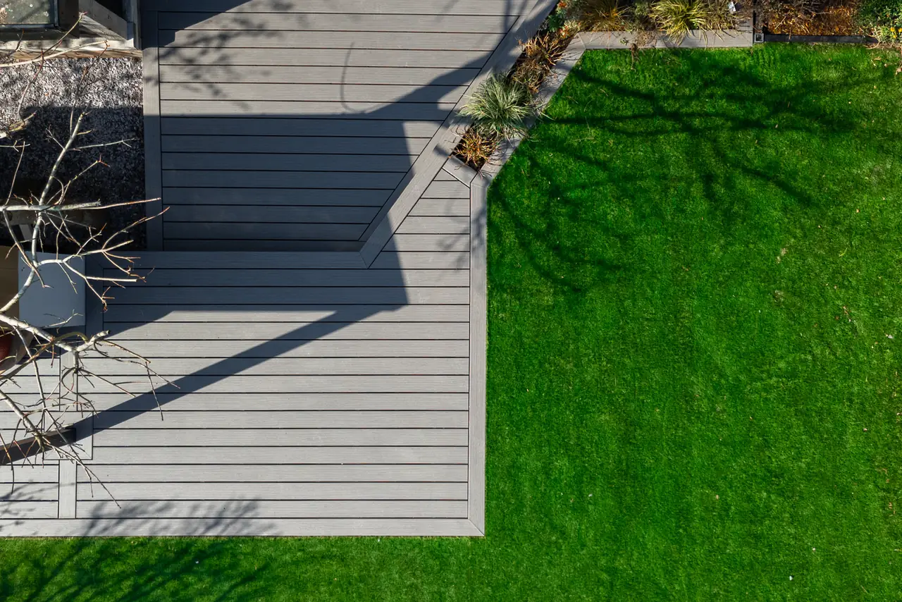 Aerial view of a finished grey Trex deck beside a lawn, boards running in two directions around a planted border