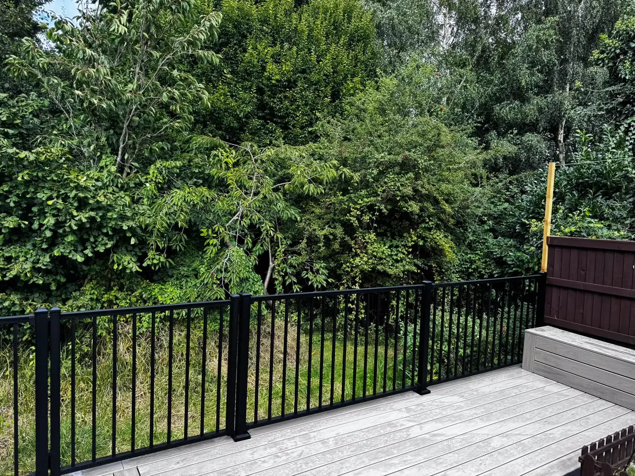 Black railing along a grey composite deck, trees behind