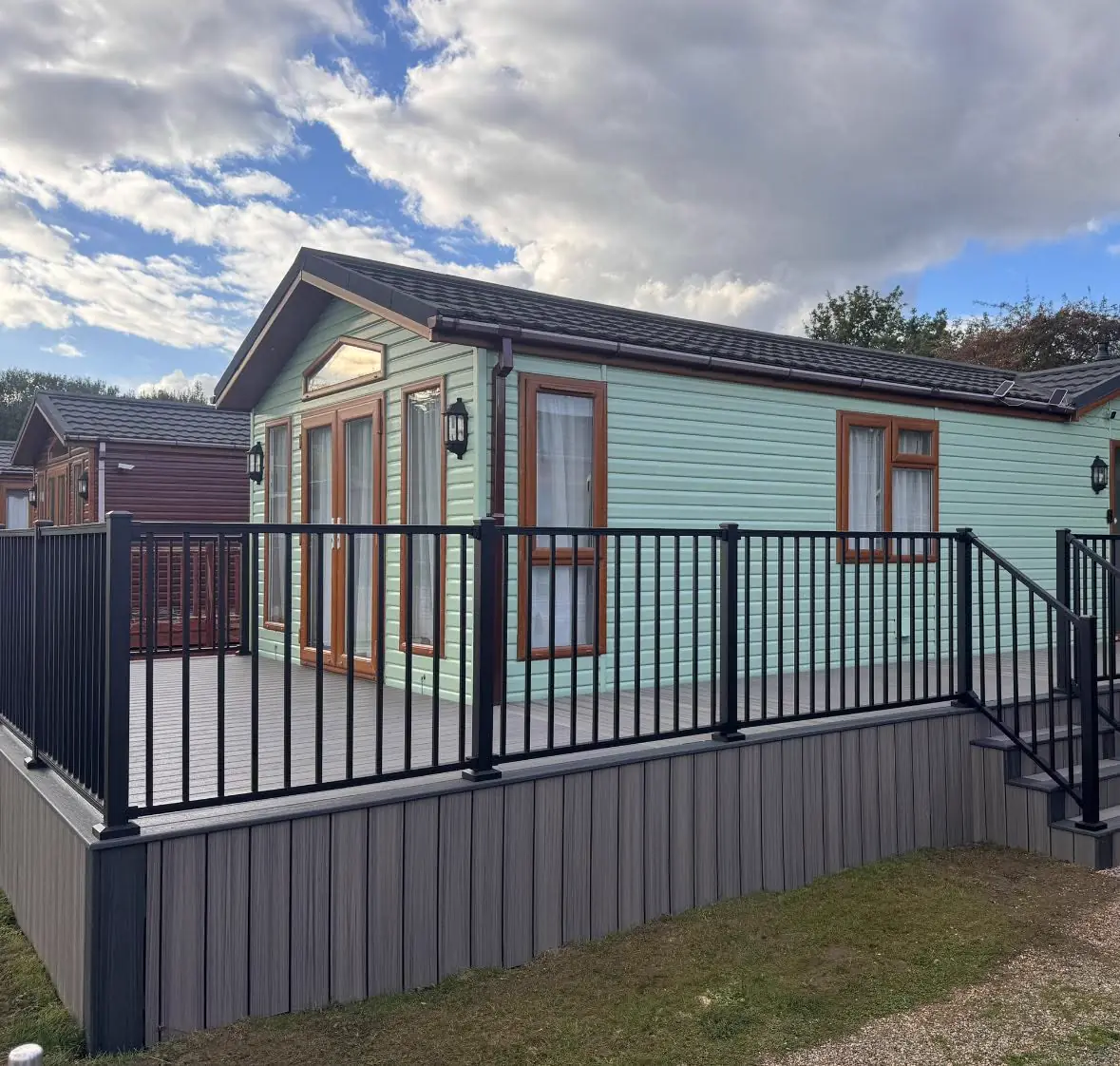 A holiday lodge with a raised grey deck and black railing