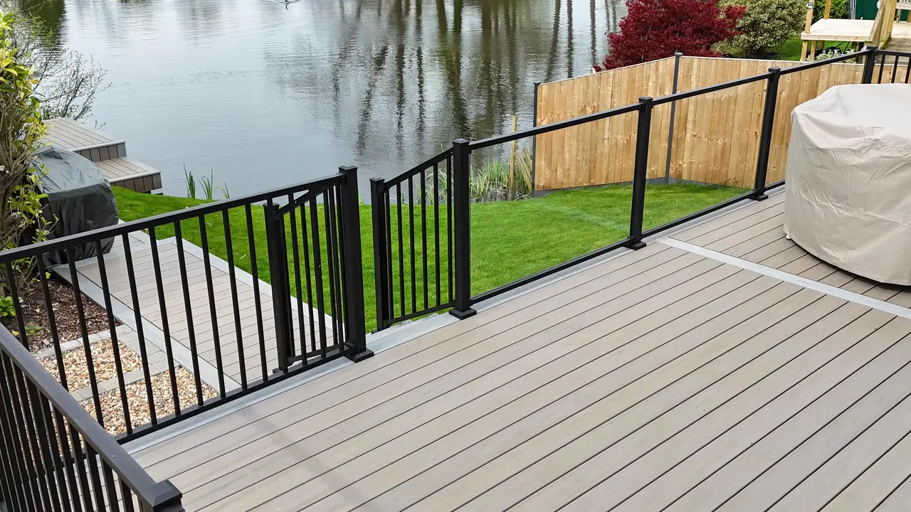 A grey deck with black railing and a gate, looking out to the water
