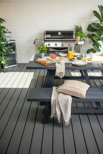 A long dining table and benches on a grey Trex Transcend deck, outdoor kitchen behind