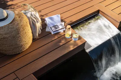 A built-in water feature spilling into a pool beside a warm brown Trex Signature deck