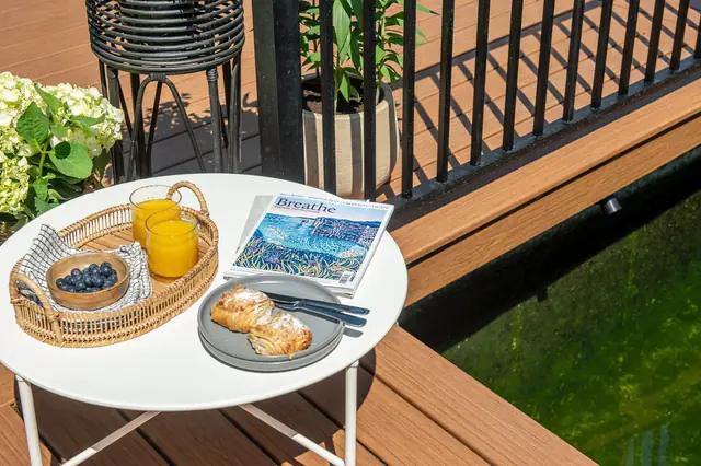 A side table on a warm brown Trex Signature deck by a black railing