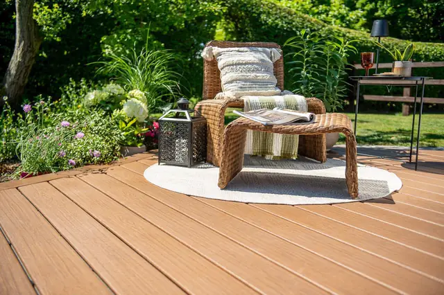 A chair on a round rug at the edge of a Trex Signature deck, planting behind